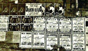 MOVIE POSTERS, ISTANBUL, 1928, By: Maynard Owen Williams, National Geographic Archive. One of the most radical reforms of Mustafa Kemal Atatürk’s Republican period was the abrogation of an Arabic alphabet in favor of a Latin one, an attempt to link the nascent Turkish Republic to the West and to break the ties of the Republic with the “decadent” Ottoman past. The change was promulgated by the Law on the Adoption and Implementation of the Turkish Alphabet, passed on 1 November 1928 in the Turkish Parliament. The Language Commission formed on the order of Atatürk for the implementation of the reform, proposed a transition period of five years, but Atatürk found it too long and reduced the period to three months. The law was implemented starting on January 1, 1929, making the use of Latin alphabet compulsory in all public communications. The movie posters above reflect the brief transition period following the alphabet reform and the photo can be assumed to have been taken in late November or December, 1928. The posters of Alhamra and Cine Magic still used Arabic script and French, whereas Taksim Bahçesi (The Graden of Taksim) and Melek (The Angel) movie theatres had shifted to Latin script still accompanied by Ottoman-Turkish in Arabic script and French.